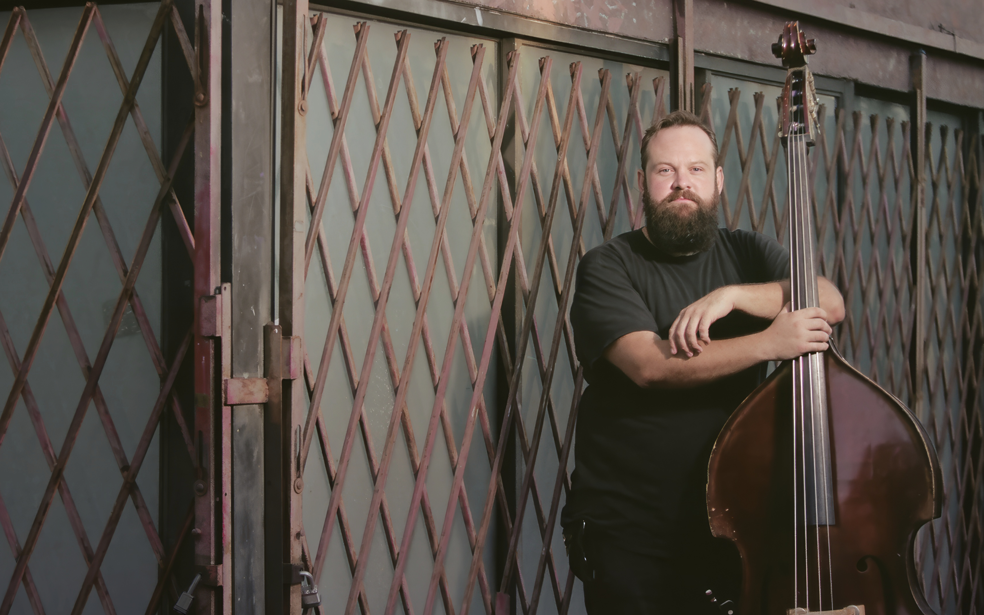 Bass legend Chris Rolontz posing for a portrait with his upright bass against a metal gate.